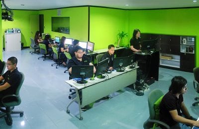 A bright, lime-green walled office with multiple people working at computers on rows of desks.