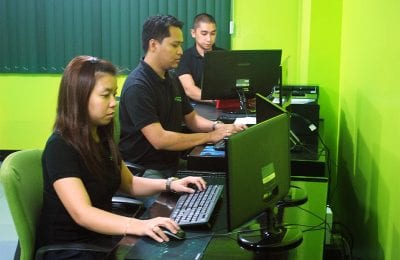 Three people sit in a row at computers with bright lime green walls in the background, facing forward.