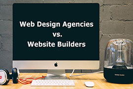 A computer monitor on a wooden desk displays the text "Web Design Agencies vs. Website Builders" with headphones and a speaker nearby.