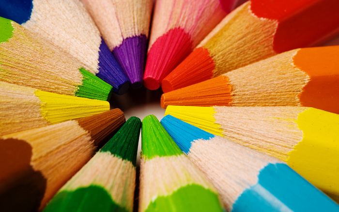 Close-up, top-down view of sharpened colored pencils arranged in a circle, their tips pointing inward to form a colorful ring.