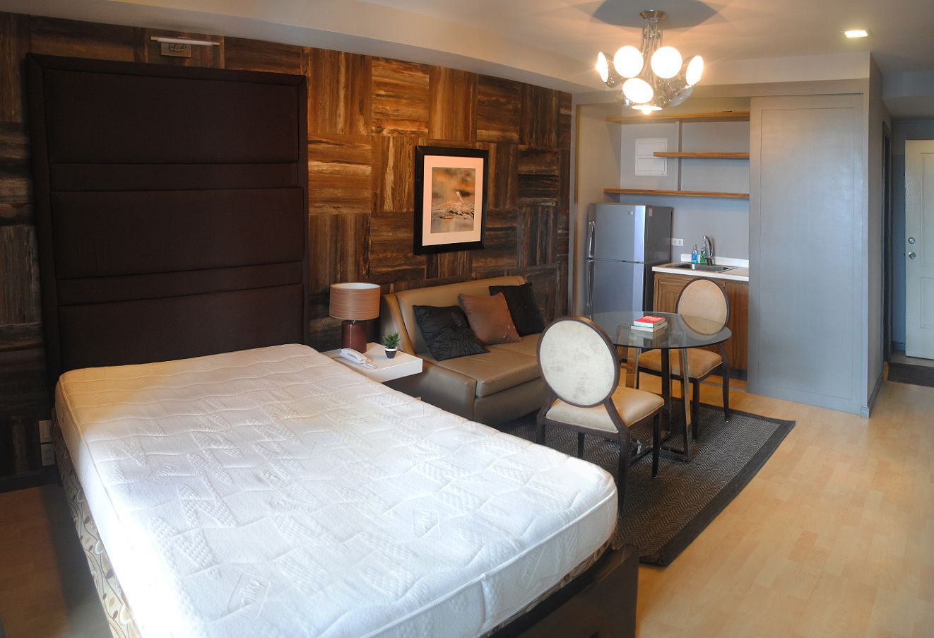 A contemporary studio apartment featuring a bed, sofa, dining table, and a compact kitchenette with a refrigerator.