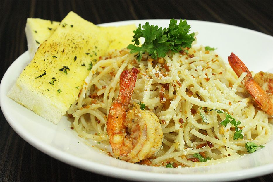 A plate of shrimp scampi pasta garnished with grated parmesan cheese and parsley, served alongside two slices of garlic bread.