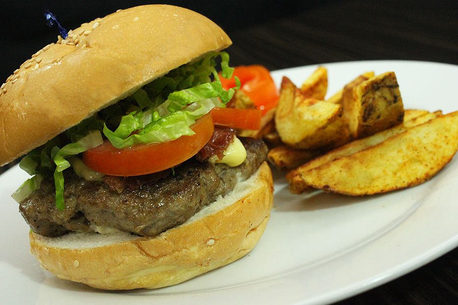 A close-up shot of a juicy burger on a white plate, served with a side of golden potato wedges.