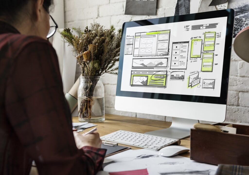 A designer sketching a website wireframe layout on a computer screen.