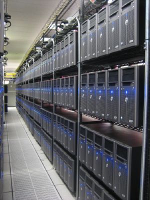 Rows of tower servers stacked on wire racks in a server room with a raised floor.