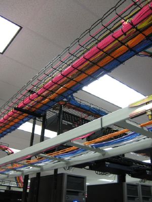 A low angle view shows rows of overhead metal wire trays carrying bundles of colorful network cables in a data center.