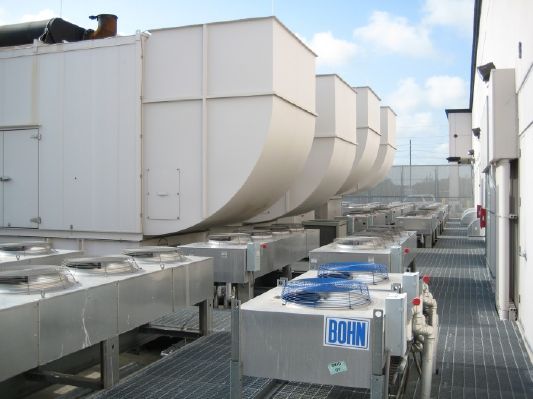 A low-angle, medium shot shows rows of large, metallic air conditioning and cooling units installed on a rooftop.