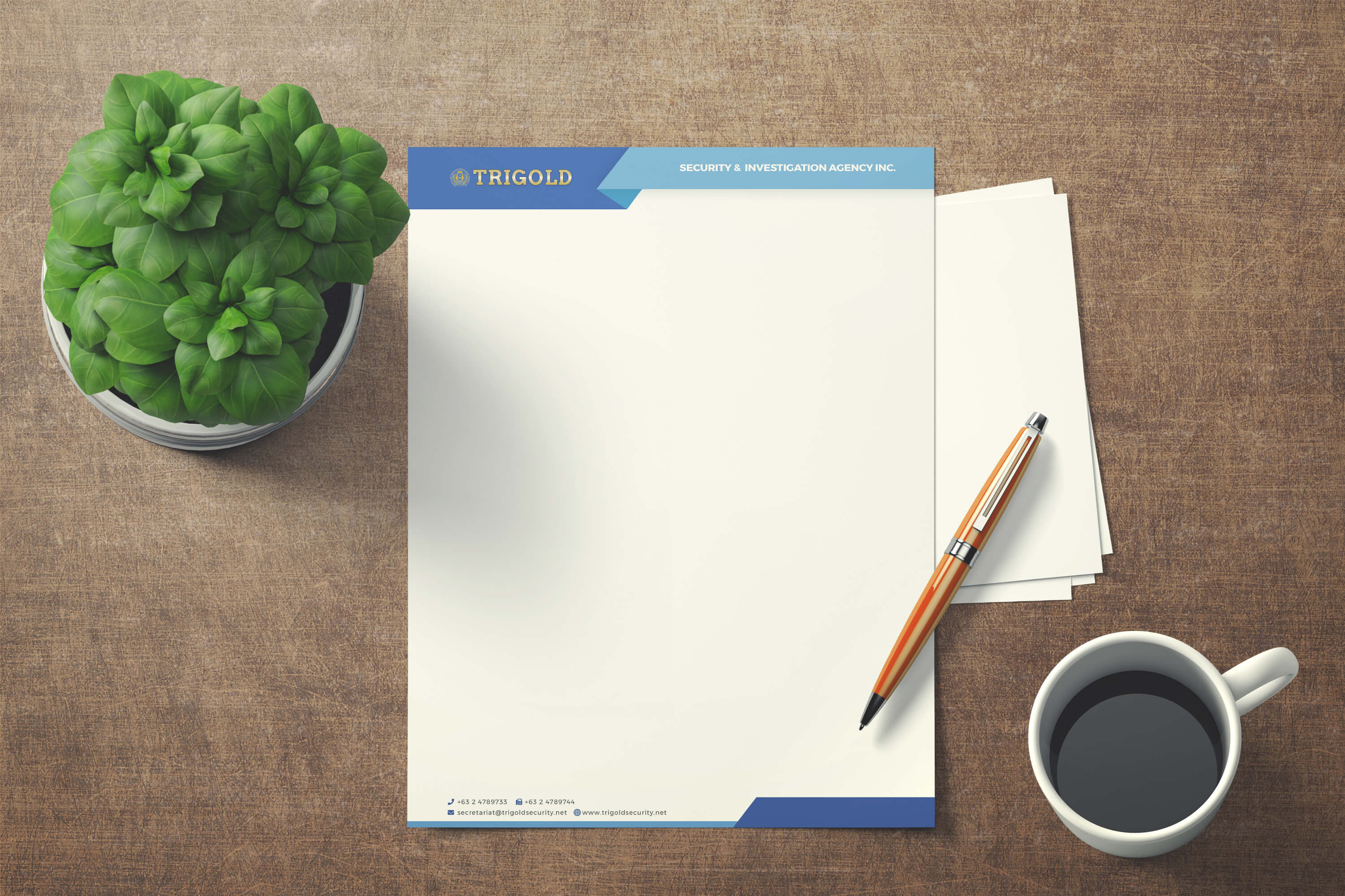 A blank Trigold Security and Investigation Agency Inc. letterhead rests on a textured brown wooden desk, next to a potted green plant, a pen, and a cup of coffee.