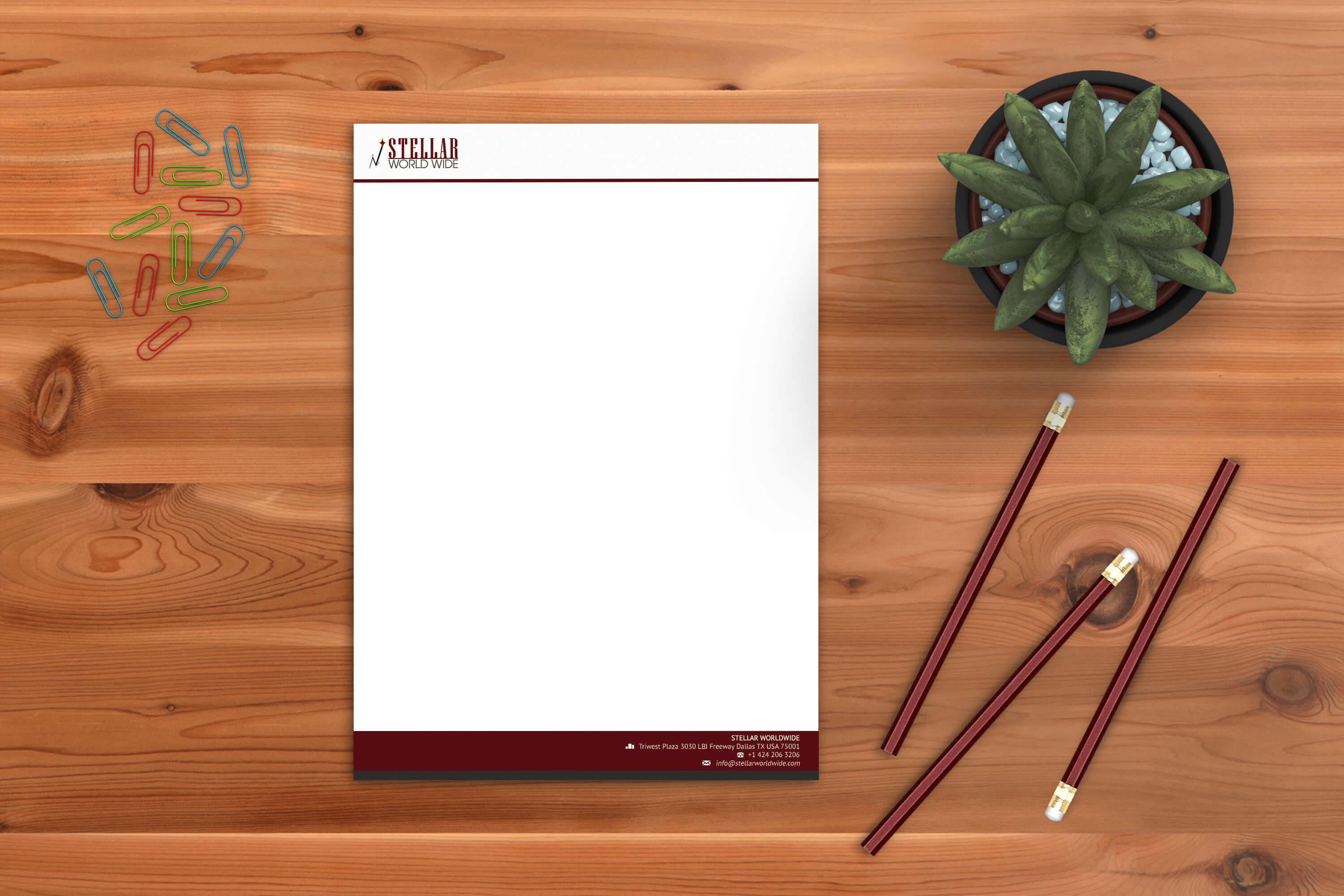 A blank piece of Stellar Worldwide letterhead rests on a wooden desk, surrounded by colorful paperclips, three pencils, and a potted succulent.