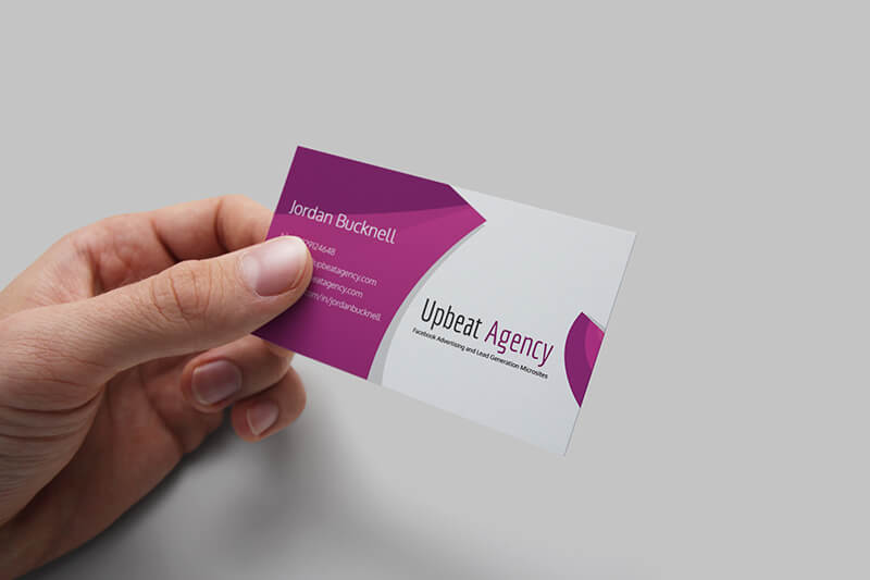 A hand holding a white and magenta business card for Upbeat Agency, featuring the name Jordan Bucknell.