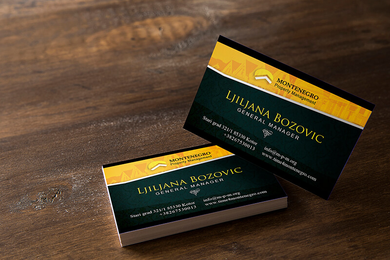 Two black and gold Montenegro Property Management business cards of Ljiljana Bozovic, General Manager, rest on a rustic wooden table.