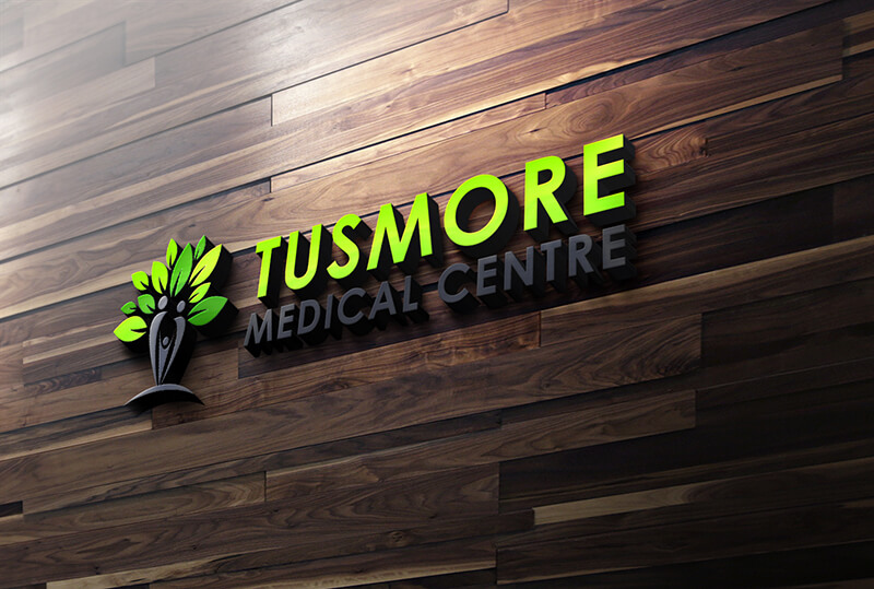 A 3D sign for Tusmore Medical Centre, featuring a tree logo with human-like figures and green leaves, mounted on a dark wood-paneled wall.