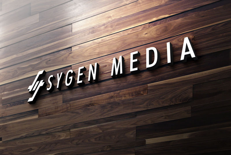 A 3D company logo reading "SYGEN MEDIA" in bold, white letters, mounted on a rustic wooden plank wall.