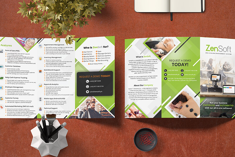 A top-down view shows an open green and white ZenSoft spa and salon management system brochure laid out on a reddish-brown surface with office supplies around it.
