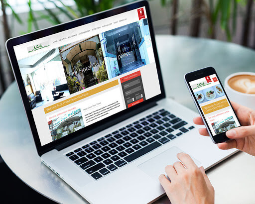 A laptop and smartphone are open on a table, both displaying the same hotel website with a responsive design.