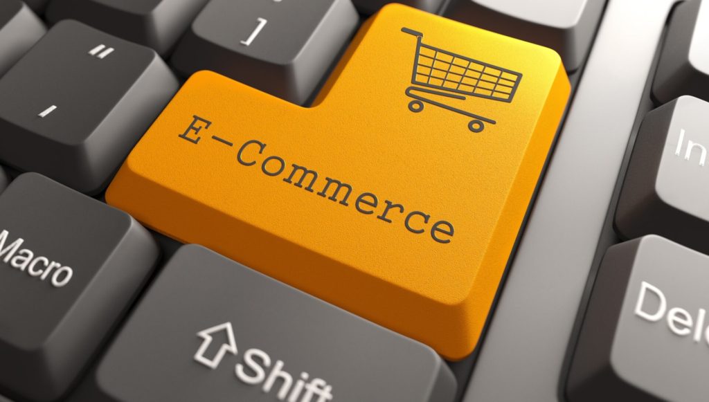 A close-up of a computer keyboard featuring a prominent bright orange enter key labeled E-Commerce with a shopping cart icon.