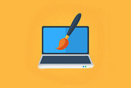 A laptop with a paintbrush on the screen against an orange background.