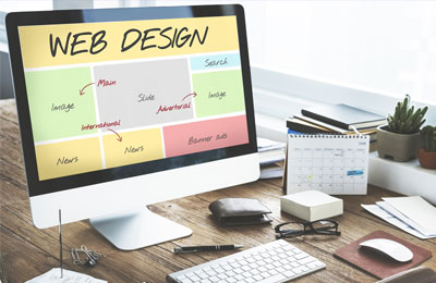 A computer monitor on a wooden desk displays a web design wireframe with colored blocks labeled for images, news, and search.