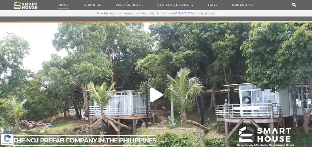 A screenshot of the homepage for Smart House, a prefab company in the Philippines, showing two elevated prefab houses set among trees and a play button overlay.