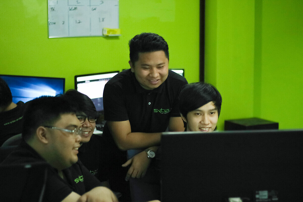 Four men collaborating in an office with bright green walls, gathering around a computer monitor.