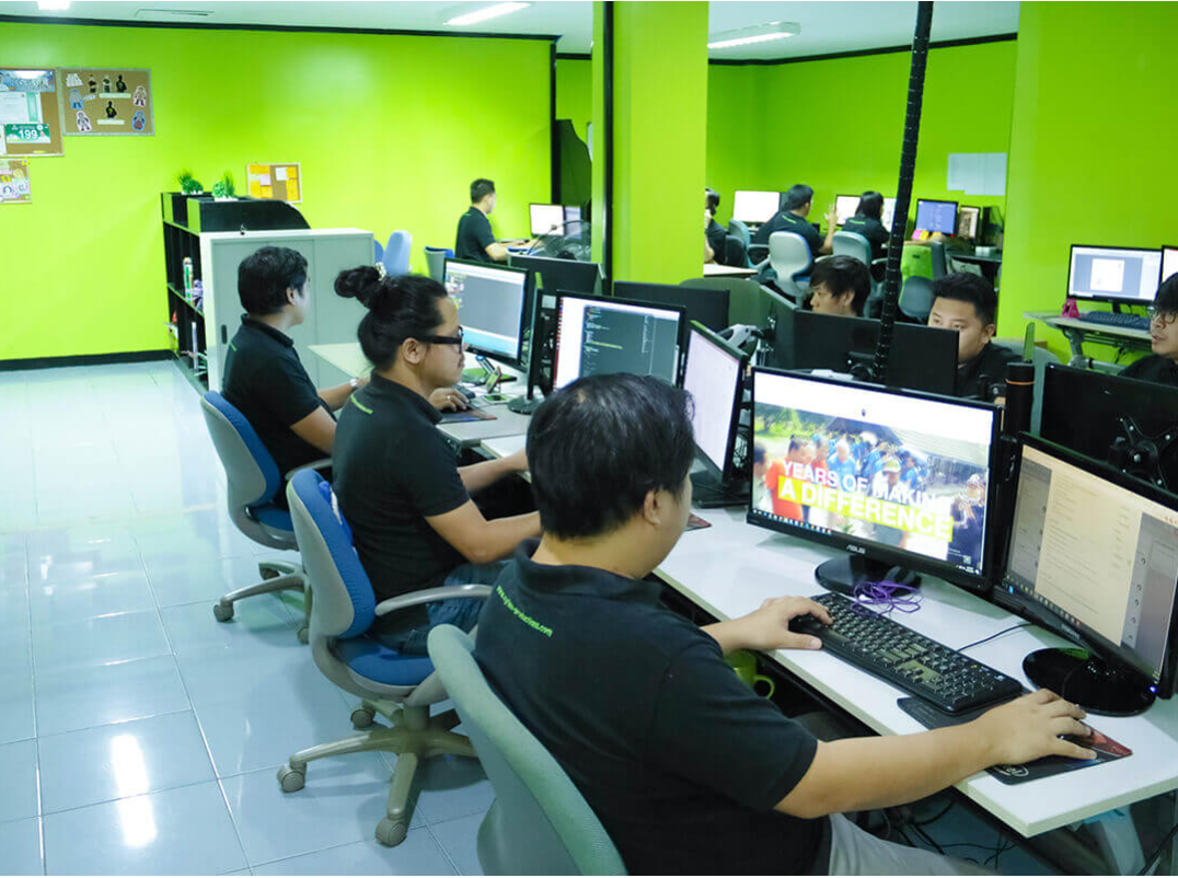 An office filled with desks and computers, with several people sitting and working on computers in the bright green room.
